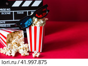 A banner for the film industry. A romantic movie date. A movie camera, 3D glasses, popcorn in striped cups on a red background. The premiere of the film. (2024 год). Стоковое фото, фотограф Photojuli / Фотобанк Лори