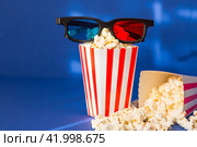 A banner for the film industry. A romantic movie date. A movie camera, 3D glasses, popcorn in striped cups on a blue background. The premiere of the film. (2024 год). Стоковое фото, фотограф Photojuli / Фотобанк Лори