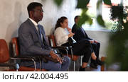 Serious-minded African male candidate siting on chair and waiting for job interview in hallway. Стоковое видео, видеограф Яков Филимонов / Фотобанк Лори
