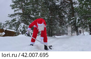 Santa Claus cleans snow with shovel in winter outdoors after a snowfall. Cleaning the streets in the village, clearing the passage for cars, difficult weather conditions for Christmas and New Year. Стоковое видео, видеограф Ольга Симонова / Фотобанк Лори