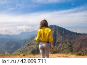 Rear view of lady enjoy at landscape Adam's peak mountain at tropical journey Sri Lanka, Ella, posing. From behind of adult woman in yellow jacket at landmark nature background. Copy ad text space. Стоковое фото, фотограф Aleksandr Golubev / Фотобанк Лори