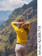 From behind of lady in yellow jacket posing at landmark nature background, Sri Lanka, Ella. Rear view of woman enjoying at landscape Adam's peak mountain. Summer vacation concept. Copy ad text space. Стоковое фото, фотограф Aleksandr Golubev / Фотобанк Лори