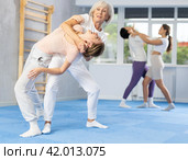 Senior woman applying inverted headlock during mock bout in self-defense training. Стоковое фото, фотограф Яков Филимонов / Фотобанк Лори