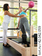 Professional Latin female instructor helping girl exercising with small pilates ball. Individual coach. Стоковое фото, фотограф Яков Филимонов / Фотобанк Лори