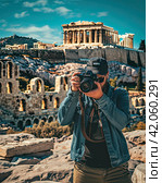 A photographer takes pictures of ancient ruins. The concept of historical tourism. The view from the back. Generated by And. Стоковое AI-изображение, AI-художник Ярославский Максим / Фотобанк Лори