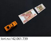 Желтая легковая машина такси едет по разметке из купюр российских денег рублей модель игрушка игрушечная черный фон. Стоковое фото, фотограф burnet / Фотобанк Лори