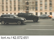Two cars in motion on city street. Racing at high speed on public road. Black Hummer H2 and Mercedes GLE SUV drive fast on urban road. Редакционное фото, фотограф Константин Григорьев / Фотобанк Лори