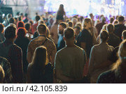People are excited during street concert. Blue neon lighting.. Young woman sits on the shoulders of her boyfriend. People make photos, video records. Night life. Street photography. Стоковое фото, фотограф YuryKara / Фотобанк Лори