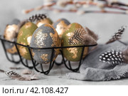 Stylish beautiful Easter eggs with golden enamel, willow branches and feathers on a gray background. The concept of happy Easter 2024. Стоковое фото, фотограф Photojuli / Фотобанк Лори