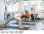 Young woman performing Utthita Parsvakonasana during group yoga workout. Стоковое фото, фотограф Яков Филимонов / Фотобанк Лори