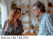 Tense Middle-Aged Couple Arguing in Kitchen, Relationship Struggles, Communication Breakdown, Divorce Concept, Emotional Turmoil, Marital Issues, Family Crisis at Home. Стоковое AI-изображение, AI-художник Оксана Гильман / Фотобанк Лори