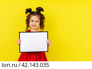little brunette girl in red drees smiling and holding an empty drawing Board, space for text,isolate on a yellow background. Стоковое фото, фотограф Ирина Михайличенко / Фотобанк Лори