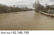 Muddy river water during a flood after heavy rains and melting snow in the mountains. River bank with people in the background. The river is about to burst its banks. Flooding. Natural disaster. Стоковое видео, видеограф Воловодов Владимир / Фотобанк Лори