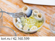 Invisible hand holds fork with pierced piece of salted herring fillet. Стоковое фото, фотограф Яков Филимонов / Фотобанк Лори