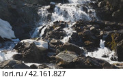 A stream of clear mountain water cascades down the rocks. A small waterfall in a mountainous area. The water foams and sparkles in the sun. The beauty of the wildlife. Front view. Стоковое видео, видеограф Воловодов Владимир / Фотобанк Лори