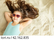 Happy cute little girl lying on a sandy beach and sunbathe in the sun. Summer travel to the sea concept. Happy smiling children. Стоковое фото, фотограф Ирина Михайличенко / Фотобанк Лори