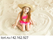 Little girl in a straw hat relax on a sandy beach and sunbathe in the sun. Стоковое фото, фотограф Ирина Михайличенко / Фотобанк Лори