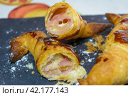 Croissant cut open revealing layers and ham and cheese filling with a shiny glaze, Sliced ham-filled croissant on a slate background sprinkled with flour, homemade croissant. Стоковое фото, фотограф carlos l vives / Фотобанк Лори