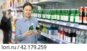 Positive woman reading label on bottle of Korean soju in Asian store. Стоковое фото, фотограф Яков Филимонов / Фотобанк Лори
