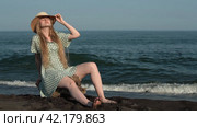 Young woman eyes closed sits on beach of black sand, straightens hat, relaxes on background of sea. Стоковое видео, видеограф А. А. Пирагис / Фотобанк Лори