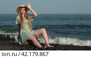 Young blonde in summer straw hat polka dots dress sits on log on shore of sea with black sand beach. Стоковое видео, видеограф А. А. Пирагис / Фотобанк Лори