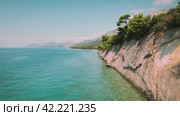 Cliffside along a calm sea, with layers of geological history. Vegetation clings to rocky outcrops above a secluded pebble beach. Aerial view of nature in summer Croatia. Стоковое видео, видеограф Igor Tichonow / Фотобанк Лори