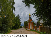 Ярославская область, деревня Веськово. Дорога к Плещееву озеру, идущая вдоль ворот церкви Георгия Победоносца в летний день перед грозой (2023 год). Стоковое фото, фотограф Наталья Николаева / Фотобанк Лори