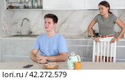 Frustrated offended guy sitting at kitchen table on background of swearing dissatisfied young wife. Family conflicts and communication problems concept. Стоковое видео, видеограф Яков Филимонов / Фотобанк Лори