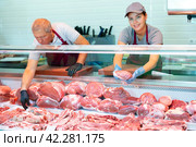 Positive young saleswoman vendor in apron and disposable gloves shows meat tenderloin. Стоковое фото, фотограф Яков Филимонов / Фотобанк Лори