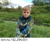 Sremska Mitrovica Serbia October 20 2021. A handsome blond boy of 8 years old in a green jacket stands on an autumn road and looks at the camera. Nature in the background. The serious face of a child. Редакционное фото, фотограф Юлия Петровская / Фотобанк Лори