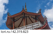 The upper part of the pagoda of a Chinese Kek Lok Si Temple against a blue sky and clouds. The curved roof is decorated with ornaments and curlicues at the edges. The spire is at the top. Malaysia. (2023 год). Стоковое фото, фотограф Вера Ивановна Кубарева / Фотобанк Лори