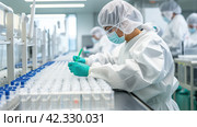 A laboratory assistant in a protective suit examines glass vials for vaccines. Medical glass vials. Close-up. Quality control. Стоковое AI-изображение, AI-художник Ирина Ручушкина / Фотобанк Лори