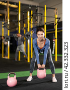 Young dedicated woman doing exercises with kettlebell near other people in crossfit gym. Стоковое фото, фотограф Яков Филимонов / Фотобанк Лори