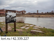 Щит со старой фотографией набережной на фоне современного места в районе замка Тапиау и реки Дейма. Гвардейск, Калининградская область (2023 год). Редакционное фото, фотограф Сергей Афанасьев / Фотобанк Лори