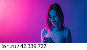 Beautiful young woman using smart phone on bright light pink background. Young igeneration, overuse, modern tech for communication, fun and leisure, AI technologies. Стоковое AI-изображение, AI-художник Alexander Tihonovs / Фотобанк Лори