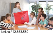 Group of curious preteen learners and young female teacher with flag of Morocco in classroom of academy. Стоковое видео, видеограф Яков Филимонов / Фотобанк Лори