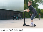 Moscow, Russia - July 26, 2019 Teenager ready to perform a trick at sportive push scooter on a city street. Редакционное фото, фотограф YuryKara / Фотобанк Лори