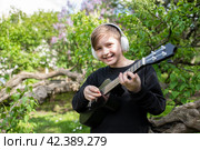 10 летний мальчик играет на черной укулеле, маленькой гавайской гитаре на природе, в парке, на фоне цветущей сирени. Стоковое фото, фотограф Яна Проничева / Фотобанк Лори