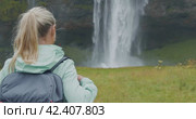 Closeup of female traveler back with backpack looking to Beautiful Seljalandsfoss waterfall Iceland. Стоковое видео, видеограф Igor Tichonow / Фотобанк Лори