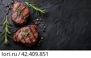Сочные стейки мяса, приготовленные на гриле, лежат на темной поверхности. Стоковое AI-изображение, AI-художник Анна Добрыдень / Фотобанк Лори