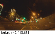 Автомобиль едет по ночному городу. Вид из салона автомобиля. Город освещен фонарями, работает подсветка зданий, светофоров. По широкой дороге едут машины. Беларусь 21 апреля 2023 года. Редакционное видео, видеограф Воловодов Владимир / Фотобанк Лори