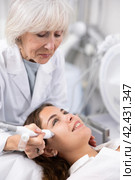 Elderly female beautician doing procedure of microneedling, mesotherapy for young woman in beauty salon indoors. Стоковое фото, фотограф Яков Филимонов / Фотобанк Лори