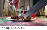 With a fork and a knife, they cut a piece of fried meat on a plate with porridge on the kitchen table. Стоковое видео, видеограф Ярославский Максим / Фотобанк Лори