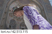 A young woman with long hair in an oriental robe and skullcap stands in the wind near an ancient mosque. Стоковое видео, видеограф Aleksey Kidisyuk / Фотобанк Лори