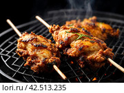 Grilled chicken. Close-up of flattened whole fried Golden crispy tobacco chicken skewered on black grill. Process of cooking meat on an open fire. Home cooking. Side view from above. Стоковое AI-изображение, AI-художник Aleksandr Golubev / Фотобанк Лори