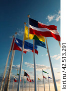 Flags different countries on high flagpoles. National flag different fluttering in wind. Flag Korea, Russia, United States, India, Vietnam, Cambodia and other against blue sky. Natural vertical photo. Стоковое AI-изображение, AI-художник Aleksandr Golubev / Фотобанк Лори