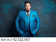 Fat chubby man with a beard in a blue three-piece suit on dark studio background, expensively dressed oligarch, tycoon, millionaire. Стоковое AI-изображение, AI-художник Станислав Тарко / Фотобанк Лори
