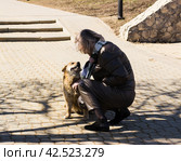 Женщина гладит бездомную собаку с желтой меткой в ухе. Липецк (2024 год). Редакционное фото, фотограф Евгений Будюкин / Фотобанк Лори