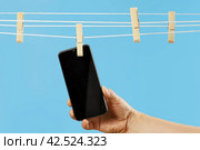 Black smartphone dries on rope of clothespin, hand holds, pure reputation. Стоковое фото, фотограф Vladimir Vikhrov / Фотобанк Лори