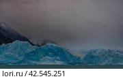 A wall of blue ice rises in a glacial lake. Melted ice floes float in turquoise water. Mountains in clouds and fog. Copy space. Perito Moreno glacier. El Calafate. Argentina. Lago Argentino. Стоковое фото, фотограф Вера Ивановна Кубарева / Фотобанк Лори